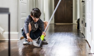 Young person in glasses uses broom and dustpan