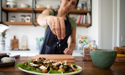 Close-up of a woman's hand sprinkling seasoning over a salad