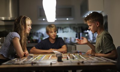 Three young people play a board game at the kitchen table