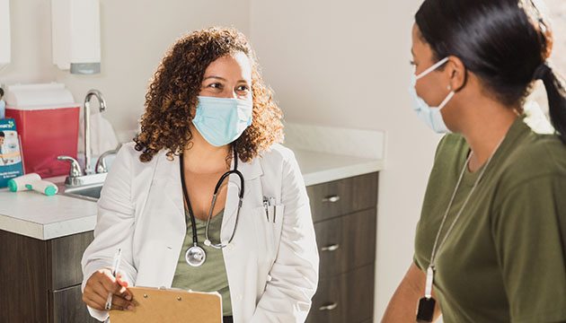 Doctor wearing a mask talks with a patient in exam room