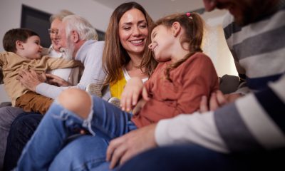 Family with two children, a parent and a grandparent laughing and smiling while sitting on a couch in the living room