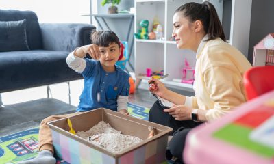 Child plays with box of sand next to a woman with a clipboard