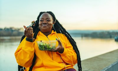 Woman wearing a yellow sweatshirt enjoying a salad near water.