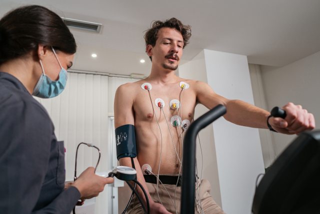 Healthcare provider stands near a man on a treadmill for heart test.