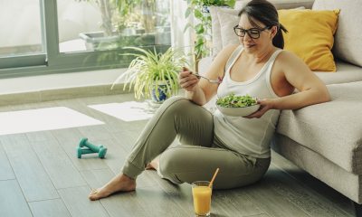 Person sits on floor next to couch, eating a salad