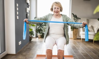 Woman sits in chair, stretching a resistance band