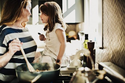 A woman and child looking away from camera while cooking at a stovetop