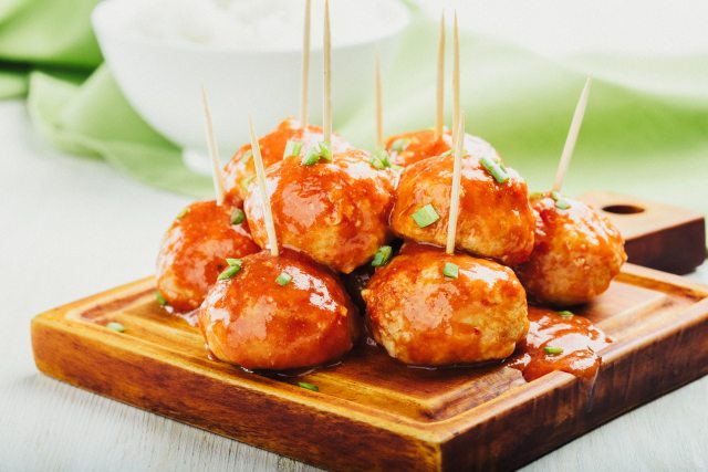 Buffalo chicken meatballs on a cutting board with toothpicks in them for easy eating.