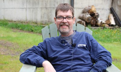 Grant Cunningham sits in a chiar in a fenced yard and smiles