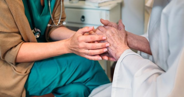 A nurse holds the hands of an older patient in a comforting manner
