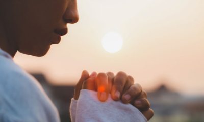 Close-up of a person with their hands folded with the setting sun in the background