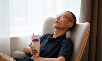 Man with glasses rests in a chair while holding a tumbler in his hand