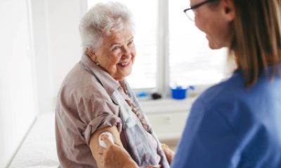Woman with white hair smiles at caregiver applying a glucose monitor to arm