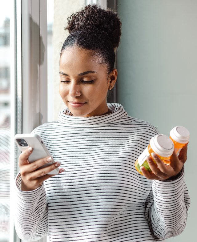 Woman holding phone and prescription bottles in her hands